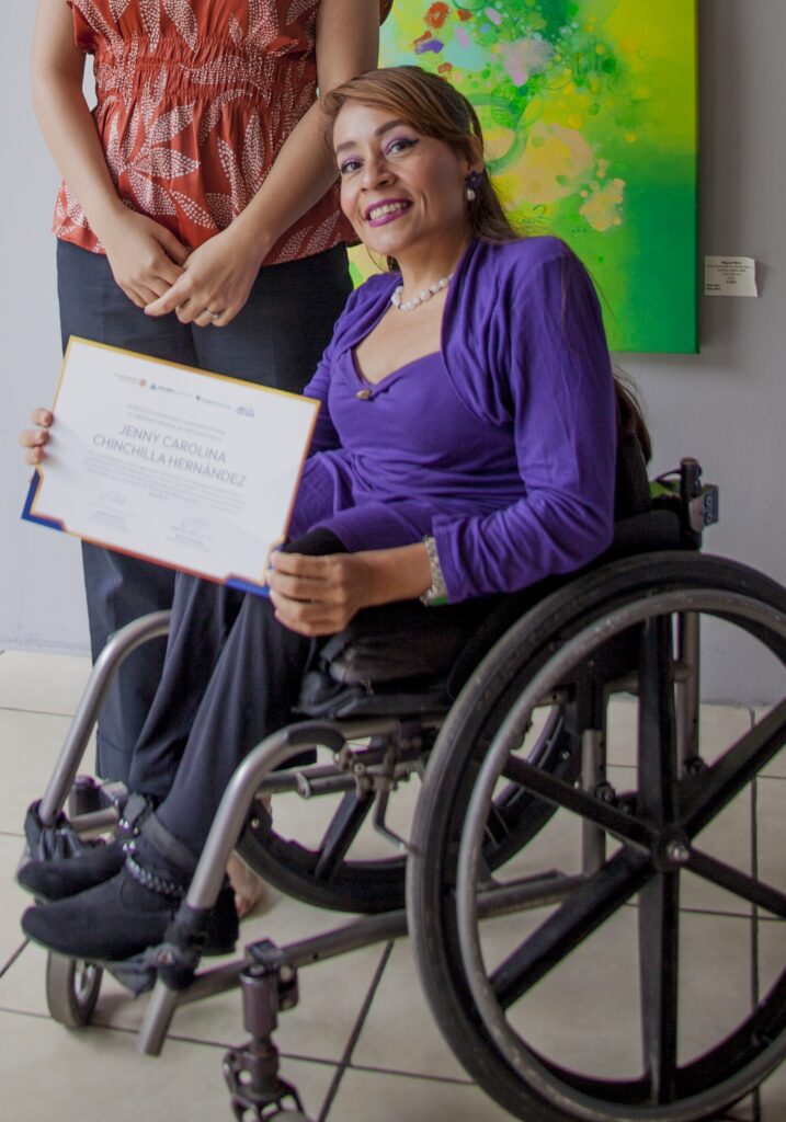 Jenny Chinchilla sitting in a wheelchair holding an award for her work supporting people with disabilities.
